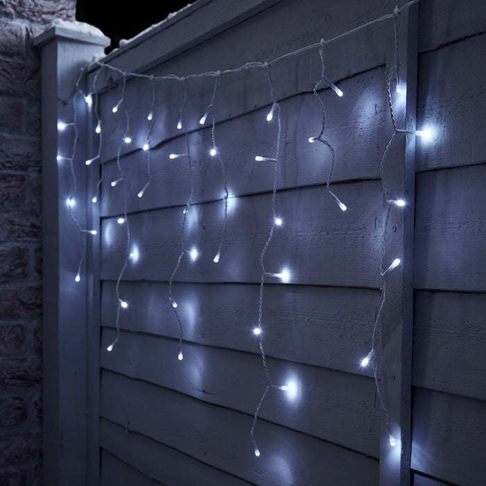 ice white lights falling in columns, hung on a fence, lit up at night