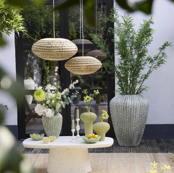 image of two hanging oval light shades, one large, one slightly smaller, hanging in a conservatory over a small table