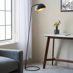 image of matt black thin floor lamp with curved head and domed shade next to grey sofa and modern brown console table