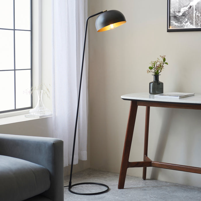 image of matt black thin floor lamp with curved head and domed shade next to grey sofa and modern brown console table