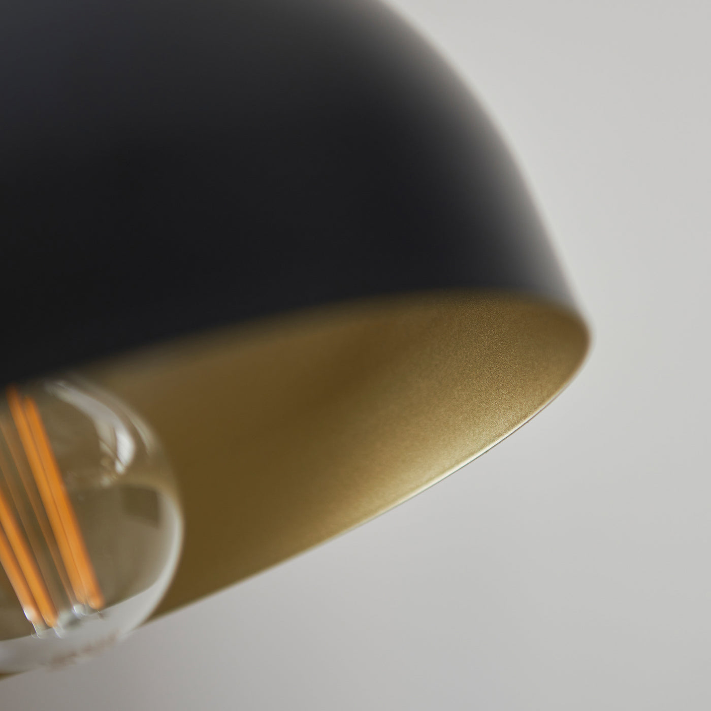close up image on bulb inside domed matt black lamp shade with antique brass inner