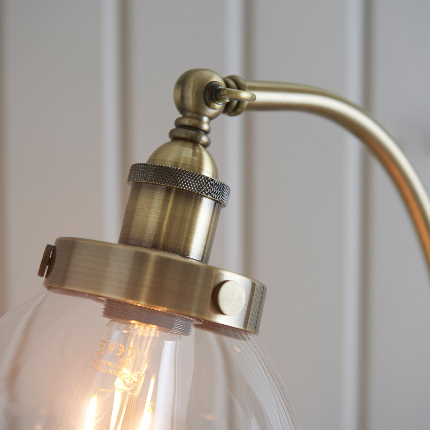 close up on antique brass fixture of floor lamp, where gently arched body meets top of clear glass shade