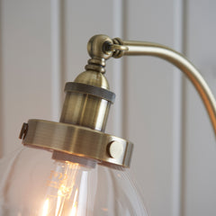 close up on antique brass fixture of floor lamp, where gently arched body meets top of clear glass shade