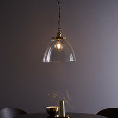 image of large clear glass light shade over warm filament bulb with antique brass fixture and hanging chain with black cable, over a dining table in front of purple wall