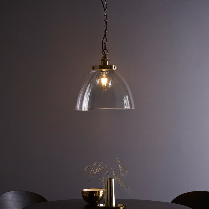 image of large clear glass light shade over warm filament bulb with antique brass fixture and hanging chain with black cable, over a dining table in front of purple wall