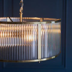 close up image of ribbed glass pendant light with antique brass metalwork edges and bulb within emitting warm glow