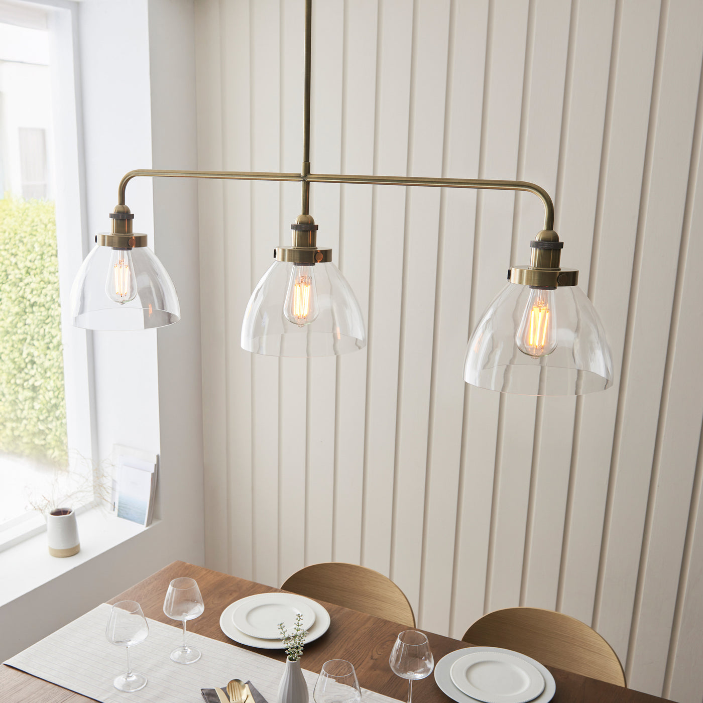 image taken from slightly above, looking down on antique brass three-set bar lights shining down on light oak dining table