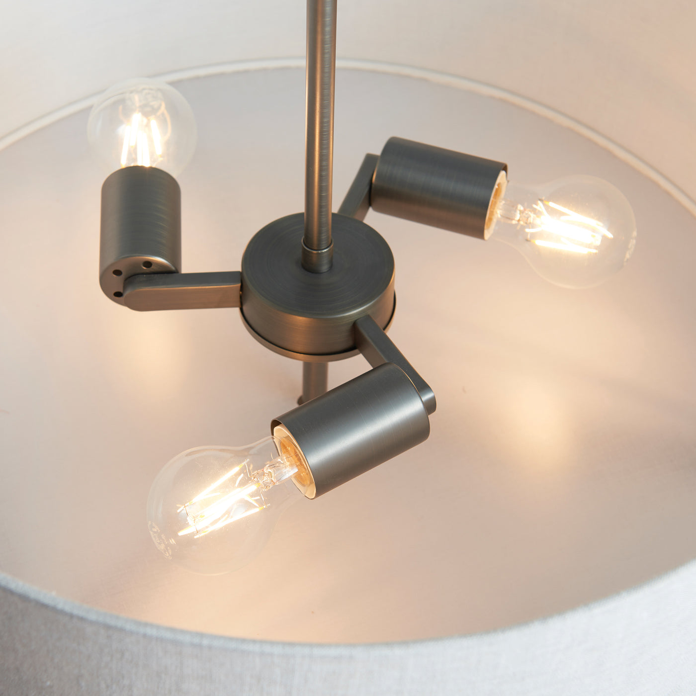 image taken from below upwards into three-pronged bronze metalwork of pendant light, showing three bulbs emitting warm light