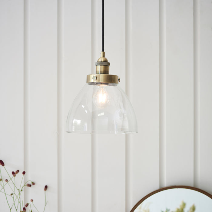 image of pendant light with clear glass shade and antique brass detail, hanging in front of cream panelled wall