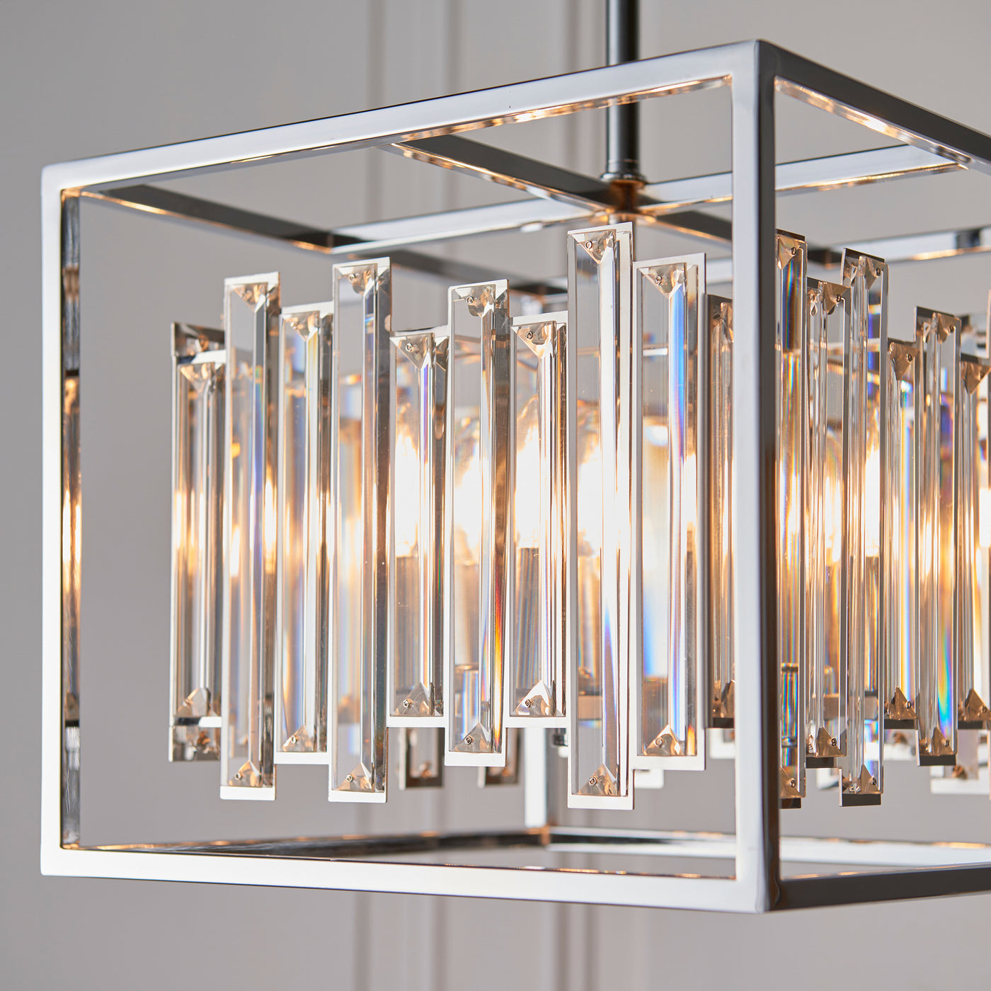close up image of chrome metal framework of hanging pendant light with abstract glass refracting warm light from within