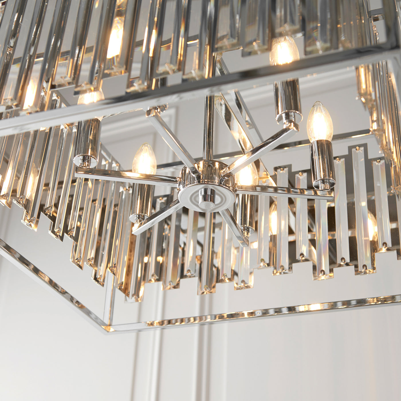 image taken from below looking upwards into large rectangular chrome ceiling light with bevelled glass sides and six candle-capped bulbs