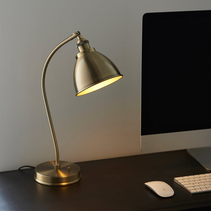 image of antique brass table lamp on a desk next to a computer, bulb switched on to emit a warm glow over the desk
