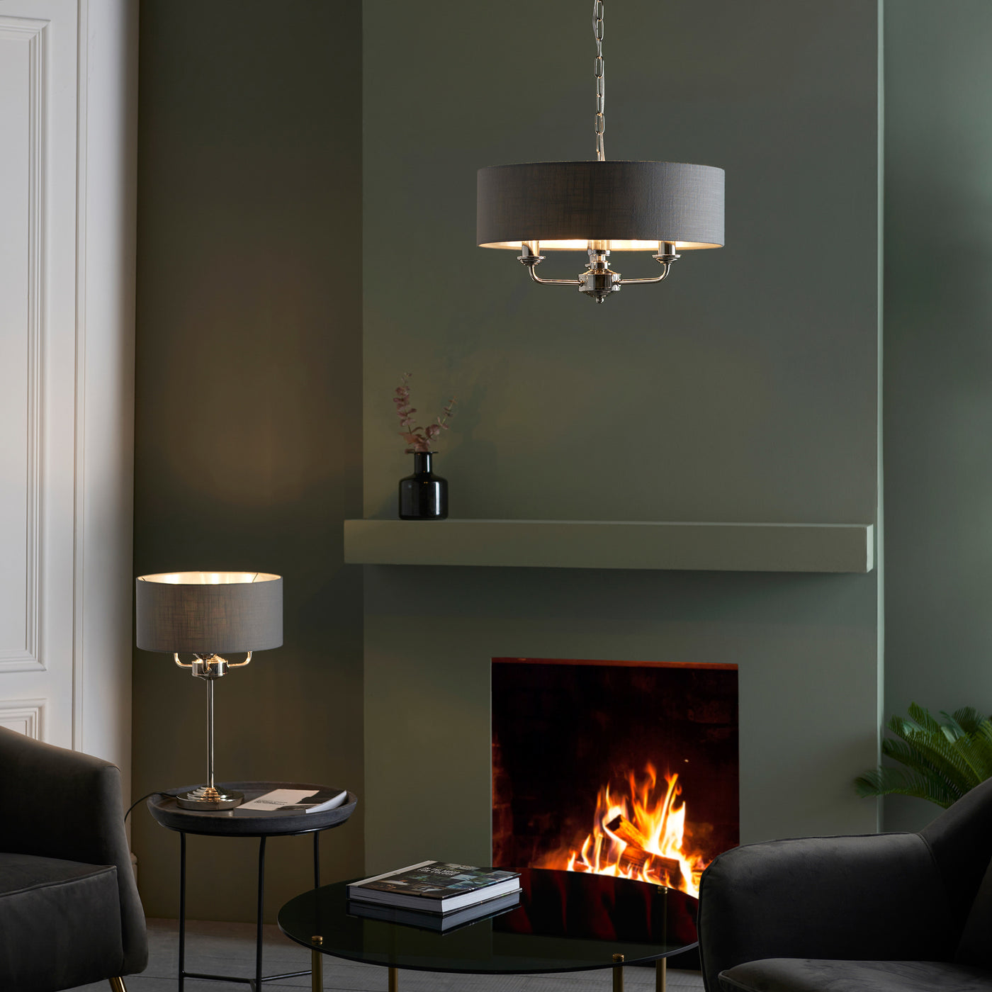 wide shot of nickel and chrome table lamp on a side table with matching ceiling light in a living room with dark green painted walls