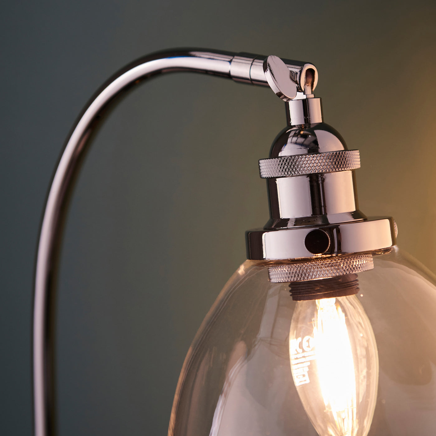 close up image of nickel fixture on top of clear glass table lamp with adjustable knuckle