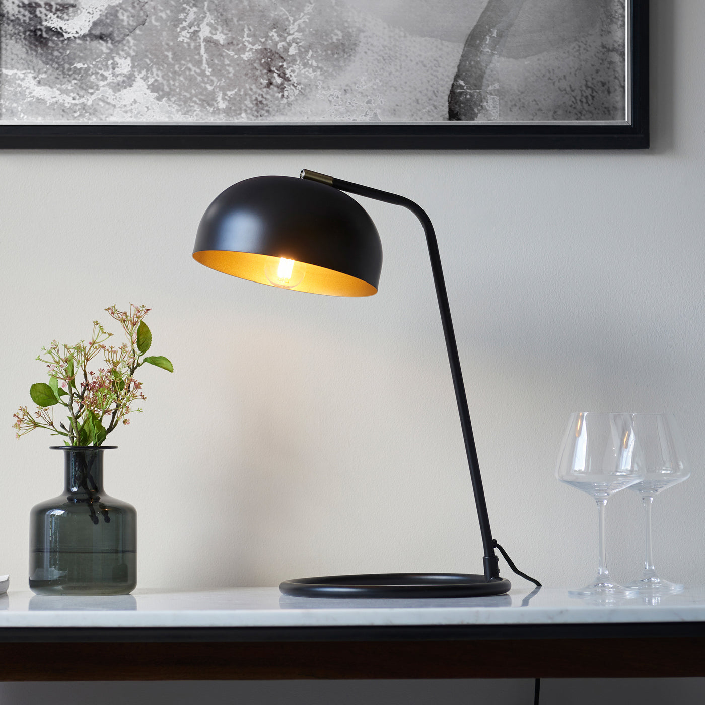 image of black table lamp with domed shade emitting warm light on a modern sideboard in front of a grey wall