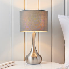 image of modern table lamp with nickel slim body with dark grey fabric shade, on a cream bedside table in front of a cream panelled wall