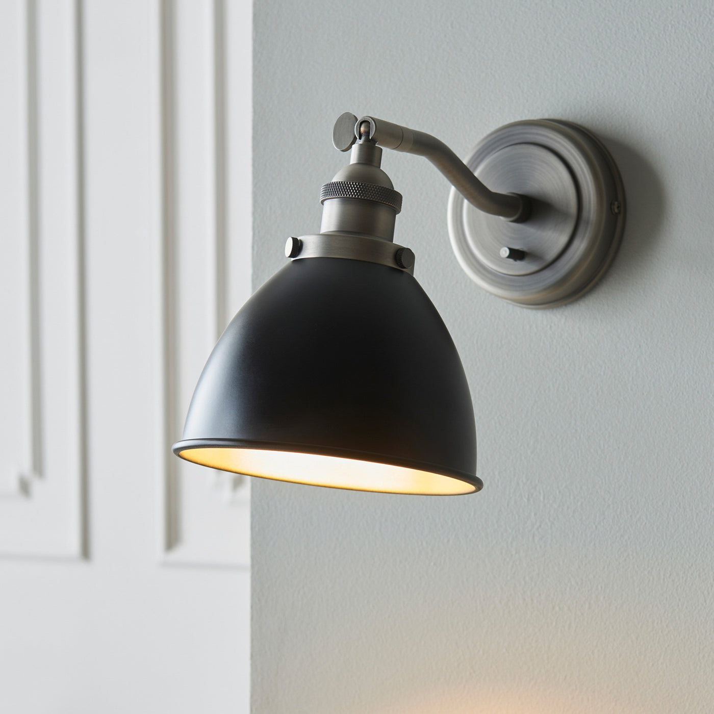 image of black and grey wall light with curved lamp head on light grey wall, bulb emitting warm glow