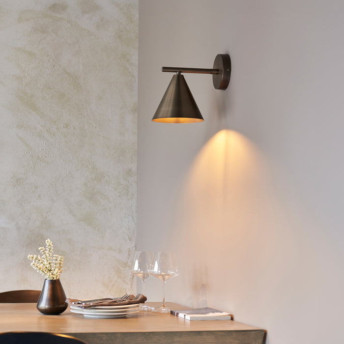 image of antique bronze coloured conical wall light on wall shining warm light onto dining table