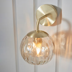 angled image of dimpled glass champagne coloured wall light against cream wall